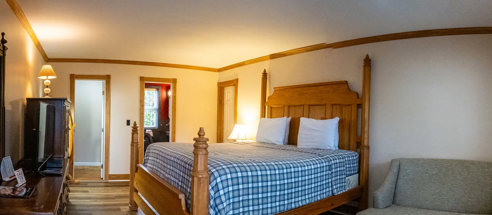 A bed with a blue plaid quilt beside a tan couch, with a hallway leading to another room in the background