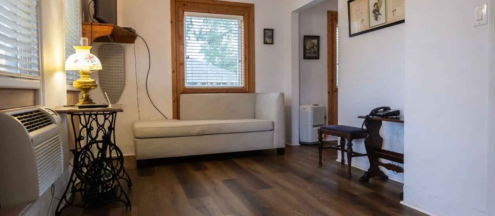 A sitting area with a beige loveseat, a sewing-machine-style side table, and a wall-mounted air conditioning unit