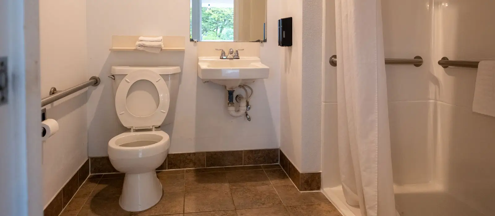 A bathroom with grab bars beside the toilet and a step-free shower with a grab bar and a fold-down seat