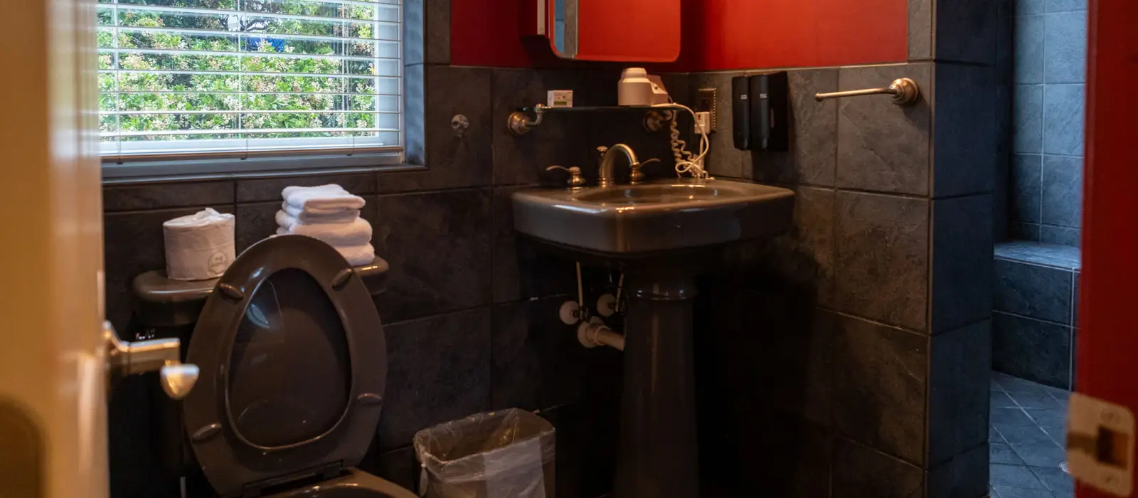 A bathroom with a dark tiled floor, a pedestal sink and a red accent wall