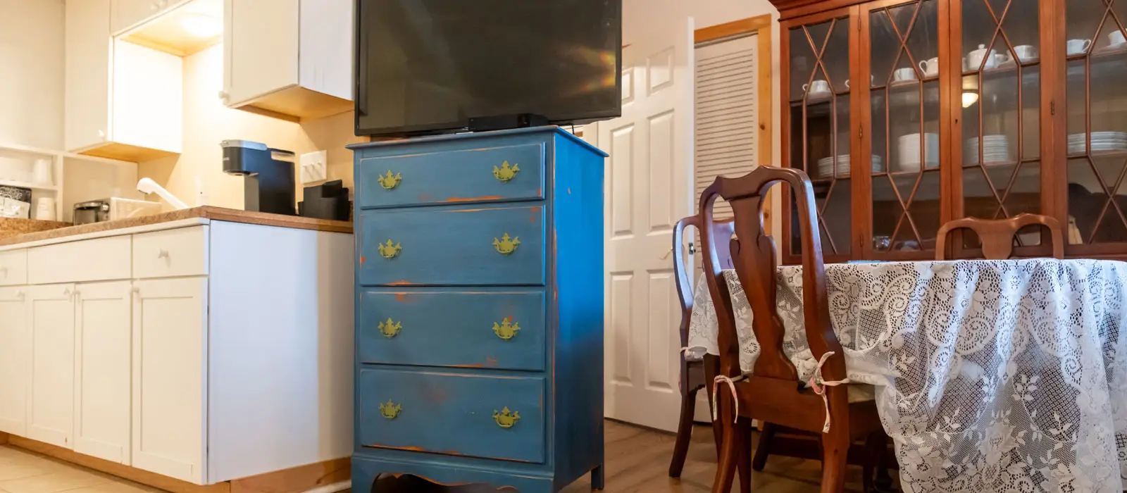A kitchenette with a coffee maker and a wall-mounted television beside a blue painted chest of drawers