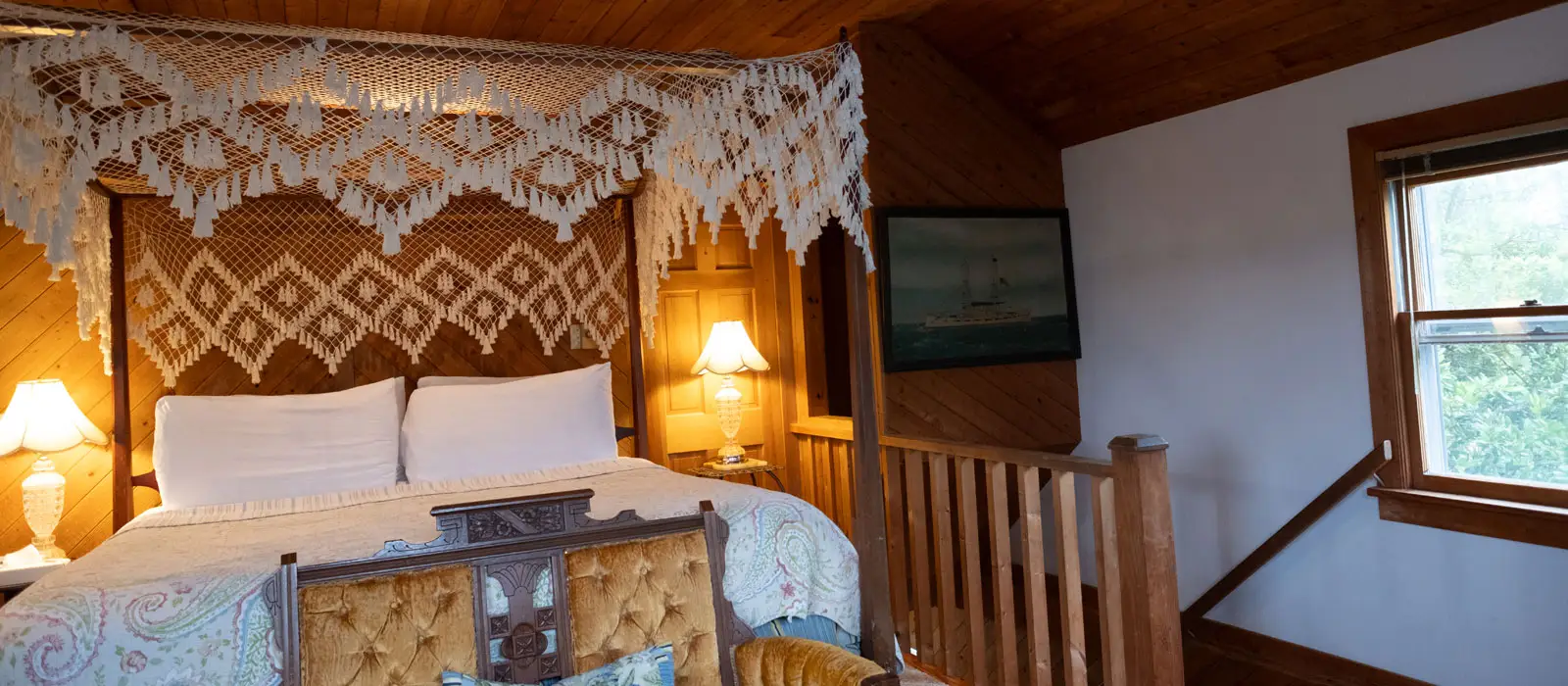 A bed with an ornate white lace canopy and a patterned quilt, lit by two bedside lamps against a wood-panelled wall