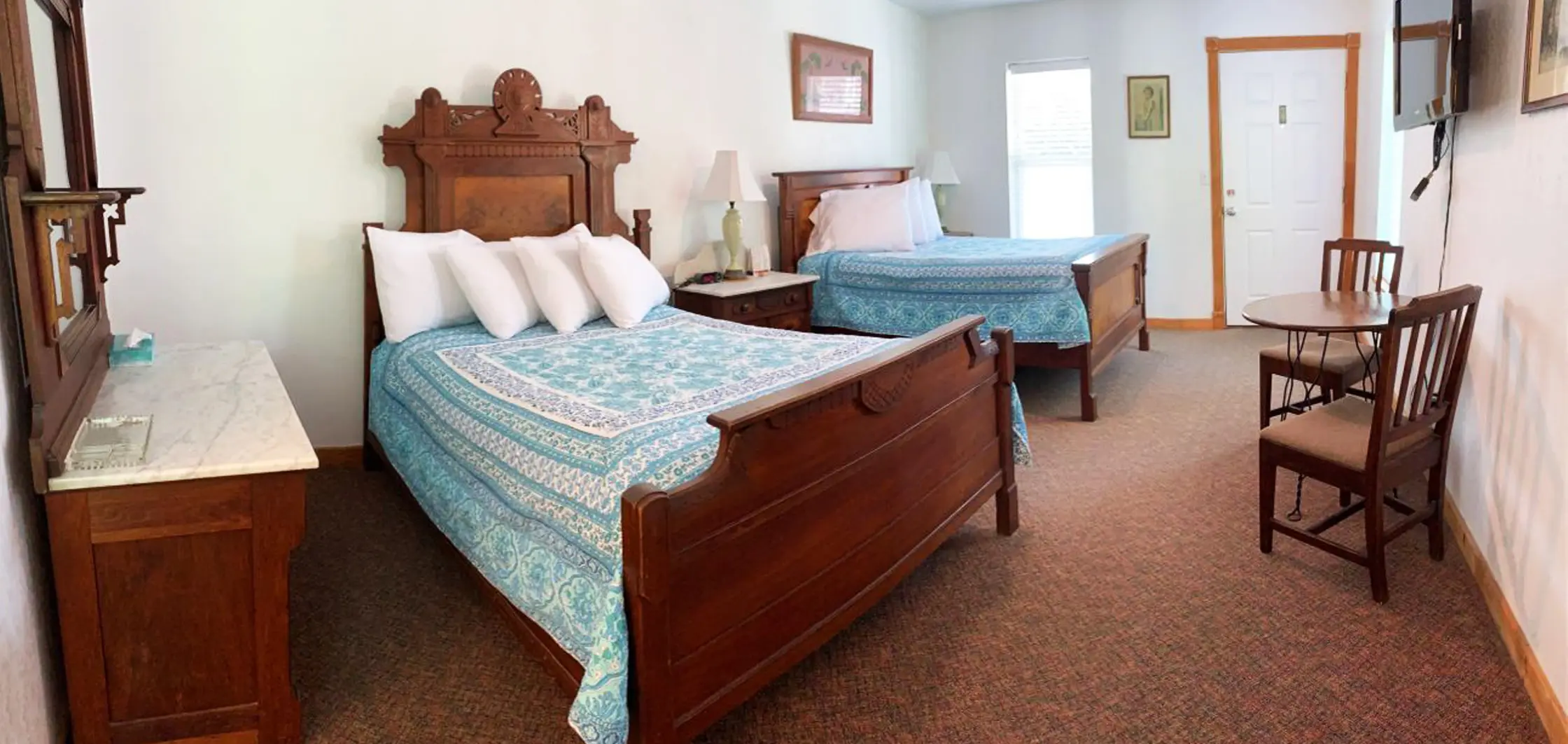 A dark wood dresser and mirror beside a bed with a teal quilt in a carpeted guest room