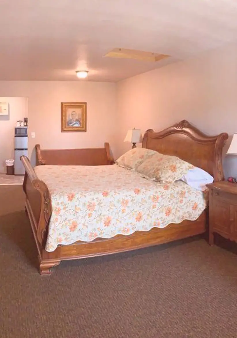 A four-poster bed with a white bedspread and floral pillow, beneath a ceiling fan and a framed picture