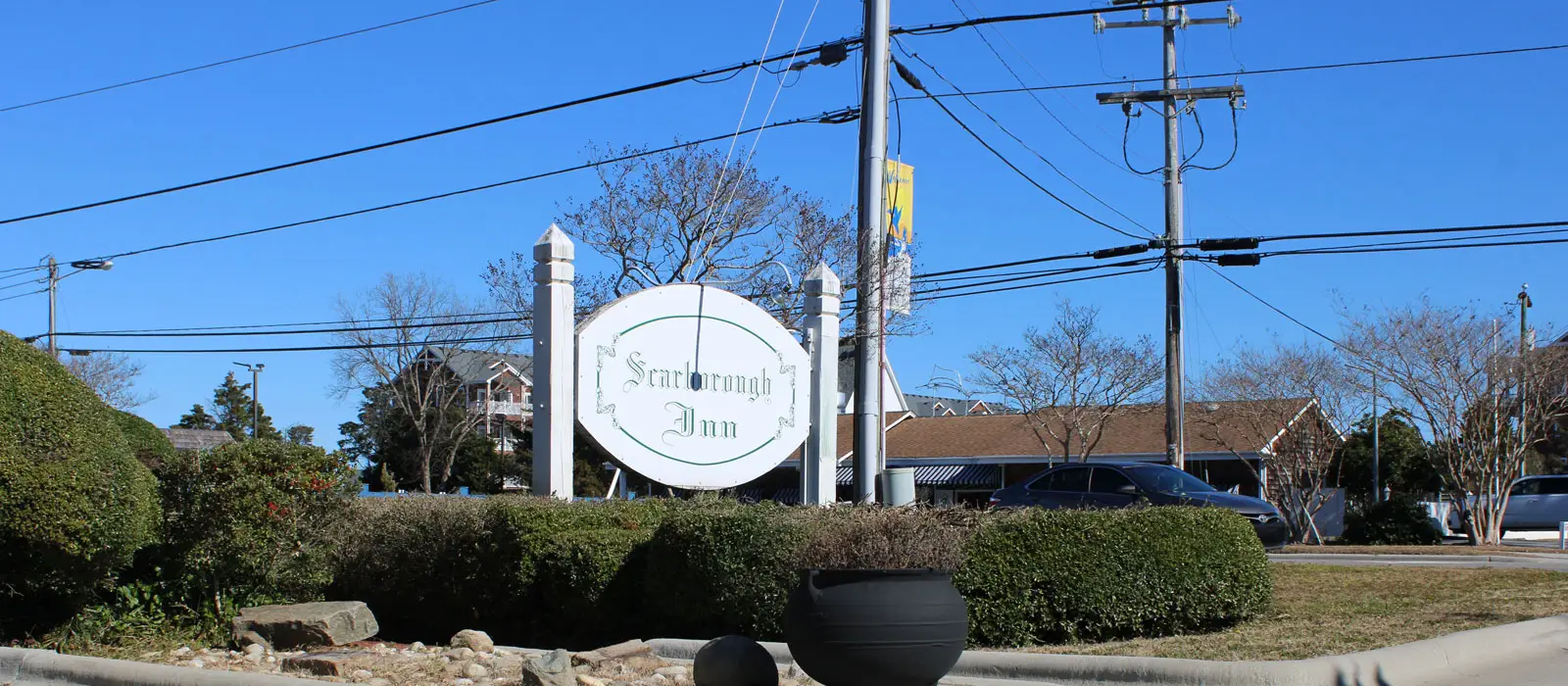 The oval "Scarborough Inn" sign on a post beside the road, with the parking lot behind it
