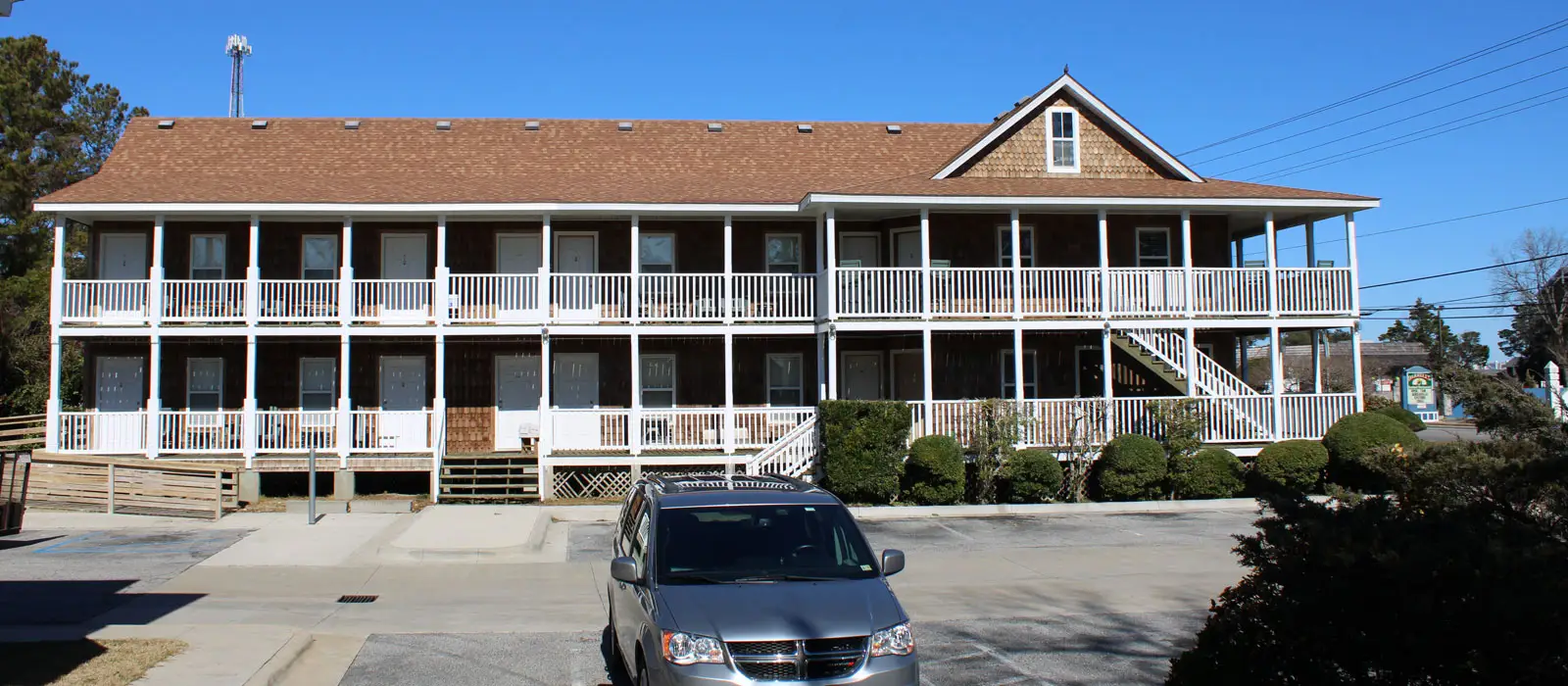 A long two-storey building with covered walkways and numbered doors along its front, with cars parked outside