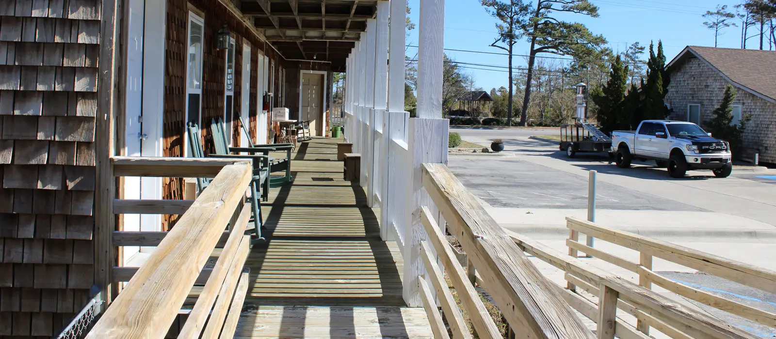 A covered wooden walkway and ramp running the length of a porch, with a parking area beyond