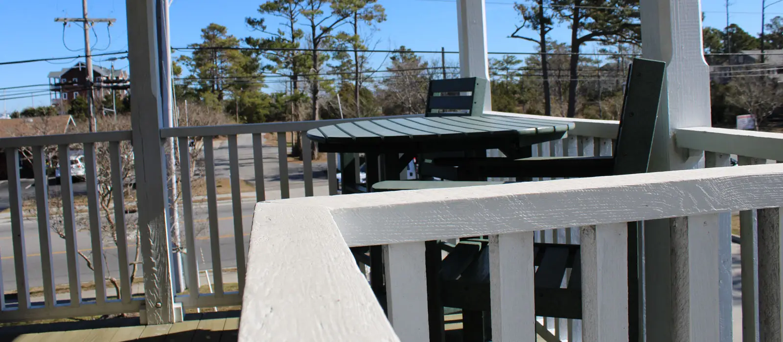 A porch table and chairs behind a white railing, overlooking a stand of pine trees