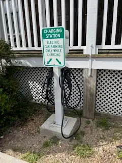 A sign reading "Charging Station, Electric Car Parking Only While Charging" beside a charging cable on a post