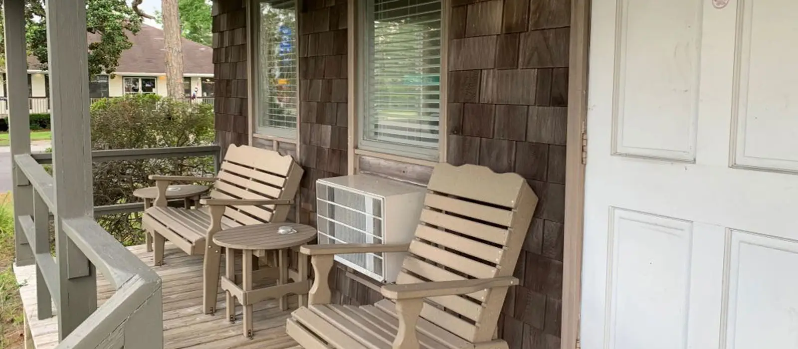 A covered porch with two wooden Adirondack chairs and a small table, against the inn’s shingled siding