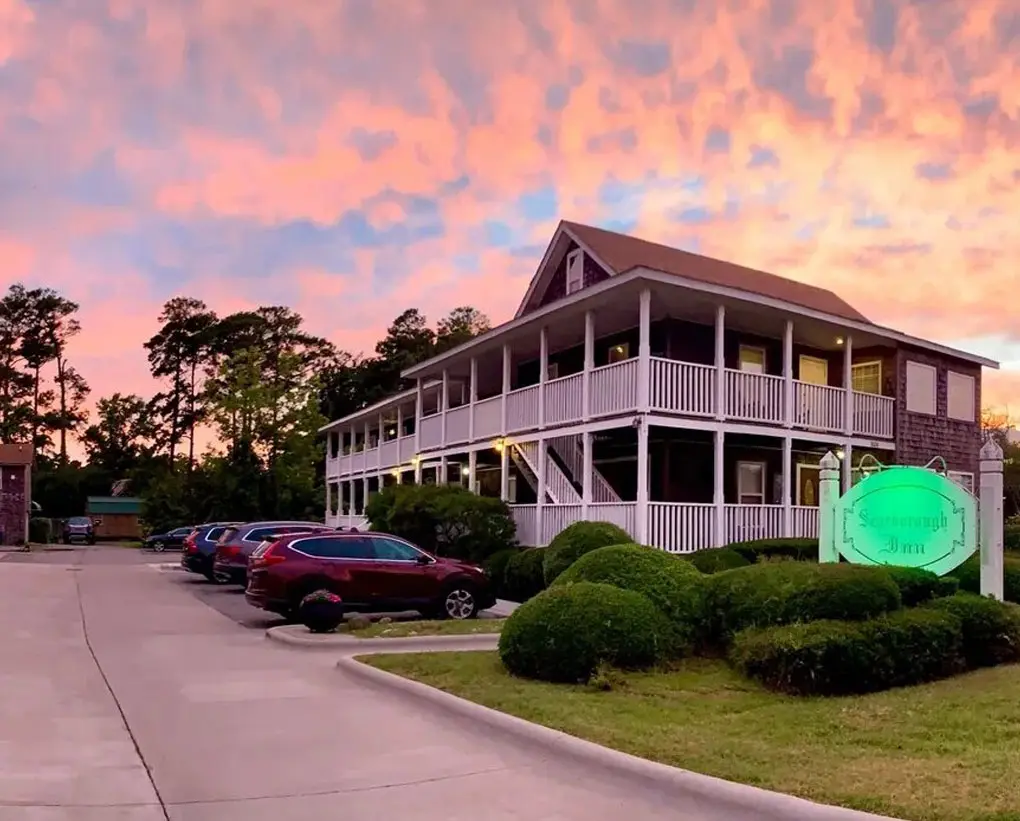 The Scarborough Inn's shingled, three-storey building with wraparound porches, lit at sunset with its illuminated sign in front