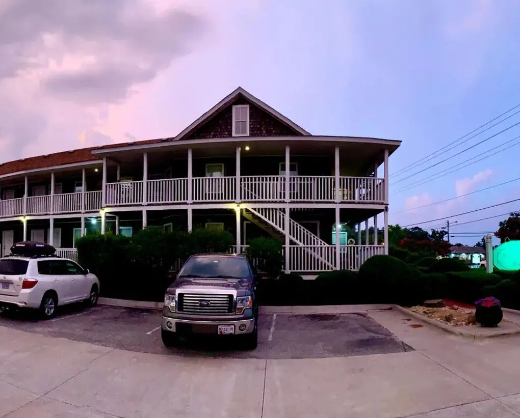 The Scarborough Inn's shingled building with a wraparound porch, photographed in daylight with two vehicles parked in front