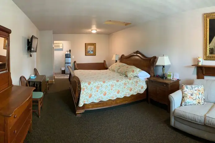 A bed with a floral quilt facing a wall-mounted television, beside a wooden dresser with a mirror